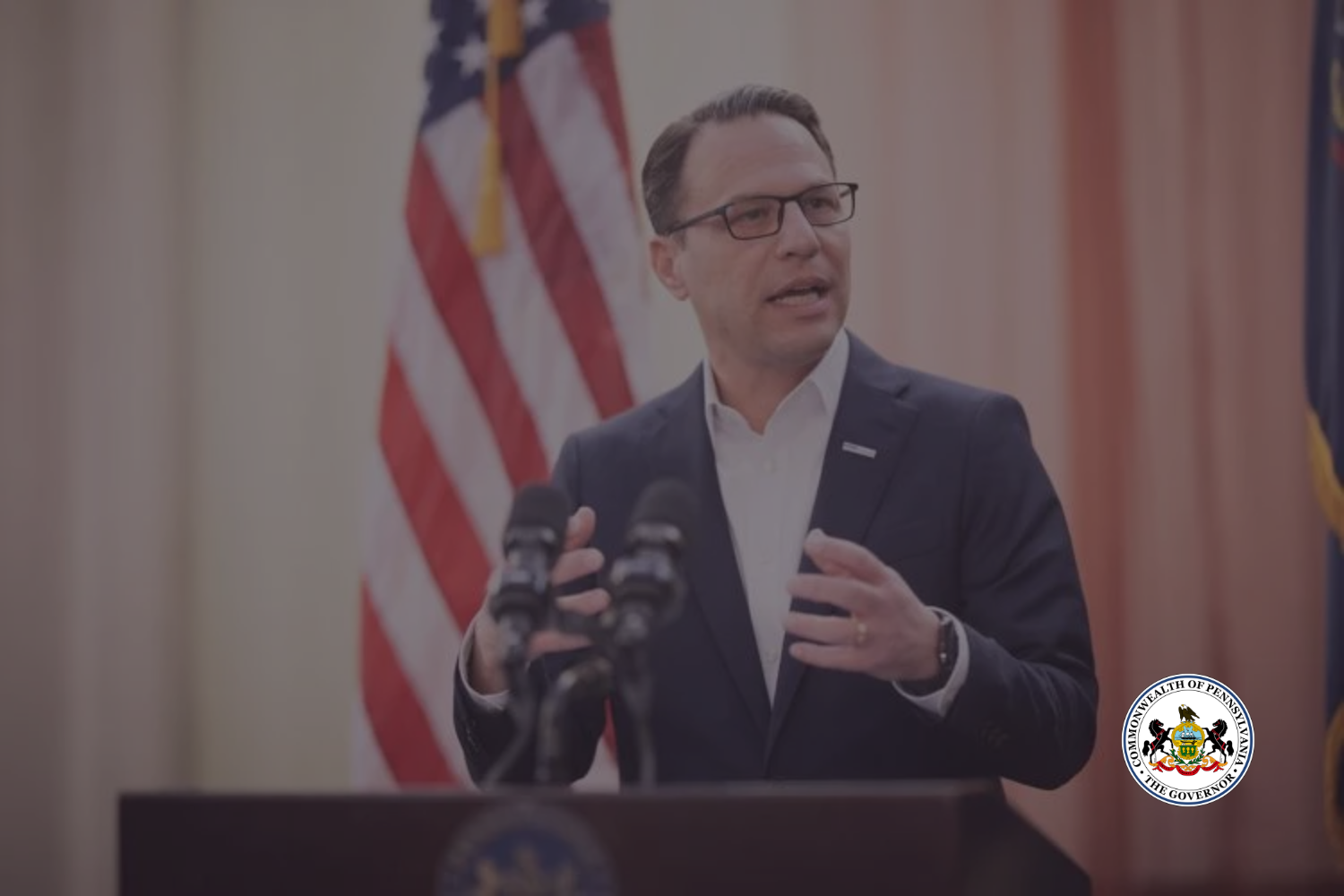 A photograph of Pennsylvania Governor Josh Shapiro, giving a speech in front of a United States flag.